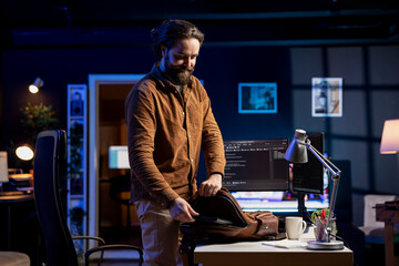 Cybersecurity specialist packing laptop after finding all security vulnerabilities and preventing malware infections. Developer putting notebook in backpack at end of job shift