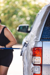 Woman washing vehicle in self-service car wash bay