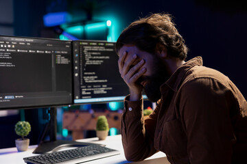 Troubled man facepalming himself while doing software quality assurance, finding major errors in source code. Depressed developer upset after inspecting coding on desktop PC and seeing many issues