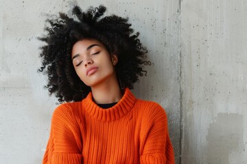 Full length of thoughtful cute ethnic woman with curly afro hair wearing vivid orange sweater with closed eyes against white modern concrete wall background - obrazy, fototapety, plakaty