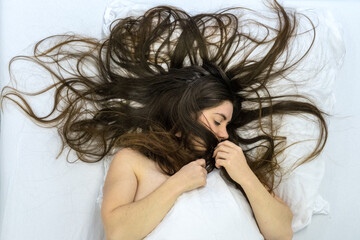 top view to attractive, young, sexy, sensual seductive nude brunette woman, long curly brown hair wild on the sheets, at sunday morning, lying in bed