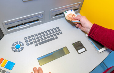 CLOSE UP OF A PERSON WITHDRAWING PENSION MONEY CASH IN EURO BANKNOTES FROM AN ATM IN A BANK.