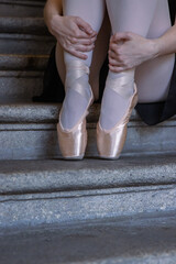 Closeup of ballerina's pointes on the gray stone steps background. Dance sitting on the stair. Ballerina is wrapping her hands around her ancles. Dancer´s feet with pink ballet slippers on. Copy space © Dina