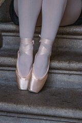 Closeup of ballerina's legs with her pink pointes shoes on. Ballet dancer is sitting on the gray stone steps. Dancer is resting on the stair. Dancer´s feet with pink ballet slippers on. © Dina