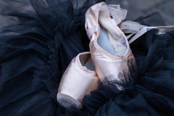 Closeup of the pink ballet pointe shoes laying on the black chiffon Tutu. Two beige ballet slippers...