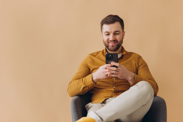 Modern millennial bearded man is happy and smiling in a yellow shirt typing something in a...