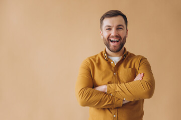 Portrait of a modern millennial bearded man happy and smiling in a yellow shirt on a beige background