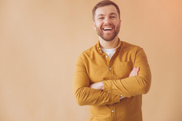 Portrait of a modern millennial bearded man happy and smiling in a yellow shirt on a beige background