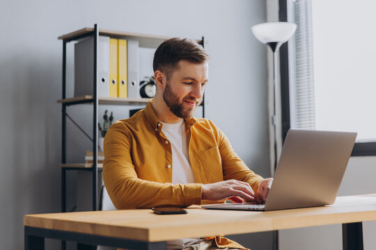 Portrait of a modern businessman man in a yellow shirt working on a laptop in the office - Powered by Adobe