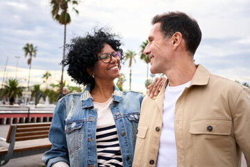 Smiling mature multiracial tourist couple embraced look at each other in love enjoying together...