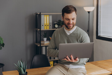 Modern happy bearded office male worker of IT company smiling and holding laptop in office
