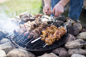 A man grills meat kebabs on an open fire on a spring day in the backyard of a private house.