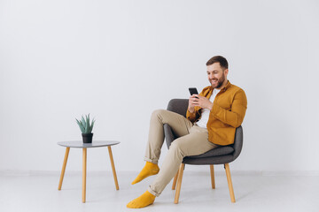Modern happy millennial man using smartphone and typing on white background