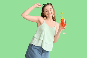 Beautiful young woman with glass of tasty aperol spritz on green background