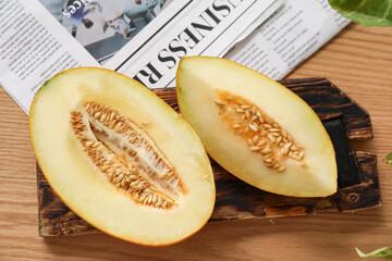 Board with cut fresh melon and newspaper on brown wooden background