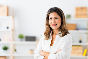 Portrait of a mature woman smiling at camera standing with arms crossed at home