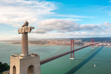 Drone flying around giant sculpture Sanctuary of Christ the King overlooking Portugal's capital Lisbon and the 25 de Abril Bridge across Tagus River. Landmarks and infrastructure in Lisbon, Portugal