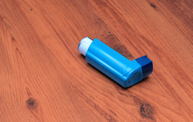 Blue asthma inhaler on wooden surface. A medical blue asthma inhaler placed diagonally on a...