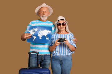 Senior couple with suitcase, world map and camera on brown background