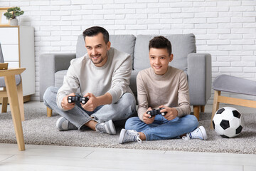 Father and his little son with soccer ball playing video games at home - obrazy, fototapety, plakaty
