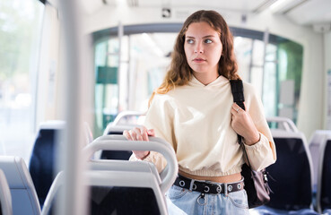 Young positive smiling woman in blue jeans traveling in tram