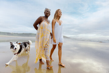 multiracial couple of female friends walking on the beach with their dogs on a summer day. Summer...