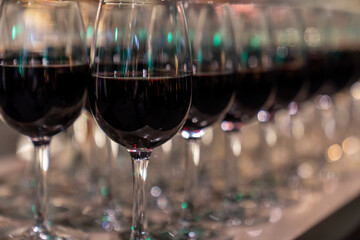 Wine glasses filled with red wine arranged and presented on a table top for self-service by party guests. Shallow depth-of-field image. A glass of red wine is on the table. Glasses of wine. 