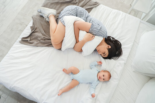 Young woman with her baby suffering from postnatal depression on bed, top view