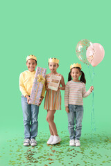 Cute little children in crowns with Birthday gift, cake and balloons on green background