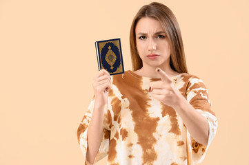 Young woman with Koran pointing at viewer on beige background. Accusation concept