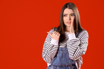 Gossiping young woman pointing at something on red background. Accusation concept