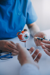 Close-up of Asian female doctor talking with elderly patient showing eyeball model and explaining eye disease in hospital