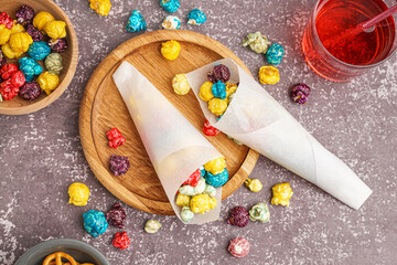 Paper cones and wooden board with sweet colorful popcorn on dark background