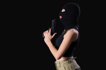 Beautiful young stylish woman in balaclava with gun on black background