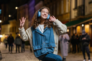 Happy overjoyed teenage girl dancing in wireless headphones choosing listening favorite energetic...