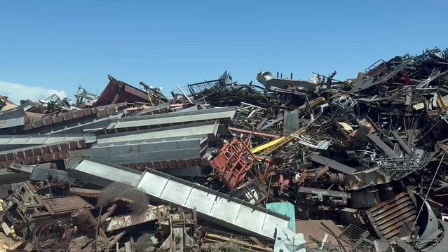 Panning shot over an industrial scrapyard. Heaps of wasted metal are being organized for recycling by heavy machinery.