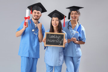 Medical graduate students holding chalkboard with text GOODBYE UNIVERSITY, diploma and EU flag on...