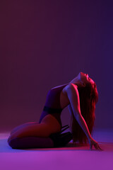 Beautiful young woman in high heels dancing on dark purple background