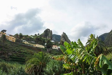 Idyllic village nestled amidst towering mountains, with vibrant banana trees swaying gently in the...