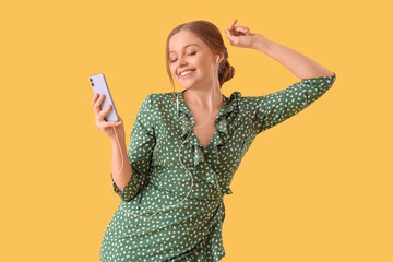 Beautiful young happy woman in headphones with mobile phone dancing on yellow background