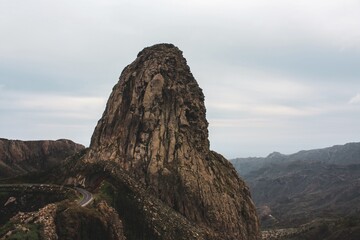 Majestic rock formation resembling a giant standing tall amidst the rugged mountains under a...