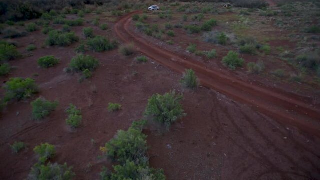 Epic drone shot over red desert with SUV's at sunset