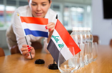 Businesswoman arranging the flags of Iraq and Netherlands for a presentation and negotiations