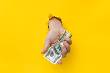 A right man's hand holds dirty money through a torn hole in yellow paper. Concept of dishonest...