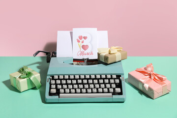 Vintage typewriter, gift boxes and postcard for Women's Day on turquoise table against pink...