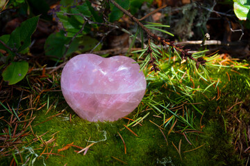 A close up image of a beautiful hearts shaped rose quartz crystal resting on a moss covered log.
