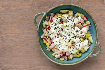 Top view of a bowl with red radish and cucumber salad with yogurt dressing and nigella seeds....