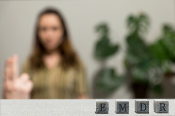 Letters EMDR written on grey stone cubes blocks. Female looking at therapist fingers in blurred background. Eye Movement Desensitization and Reprocessing psychotherapy treatment concept.