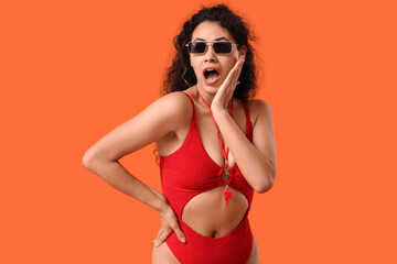 Beautiful young shocked African-American female lifeguard on orange background
