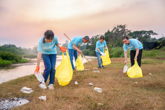 group of volunteers in blue t-shirt collecting garbage and sorting plastic waste, voluntary asian family team cleanup dirty camping area full of garbang by the river
